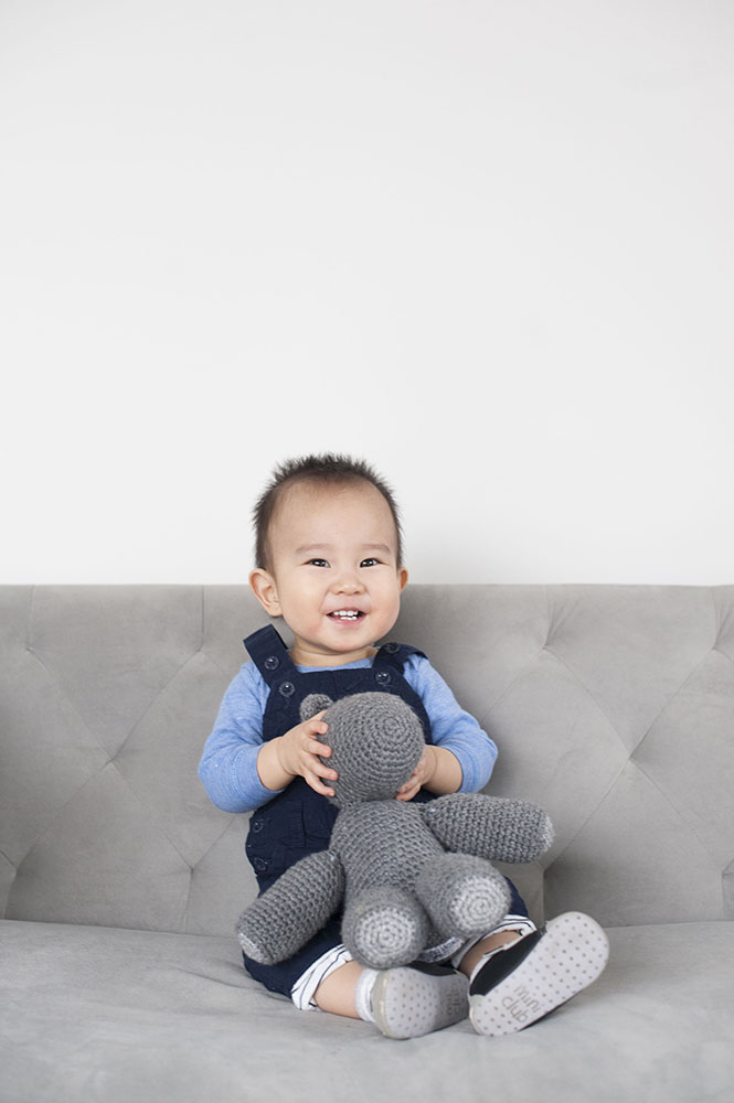 little boy on grey couch in studio with toy
