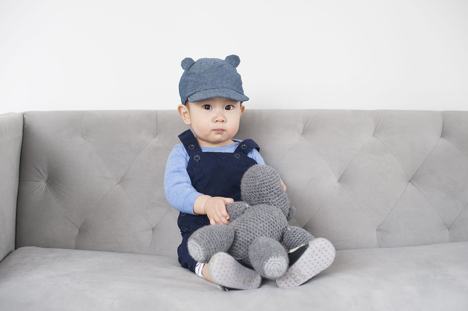 little boy on grey couch in studio with toy