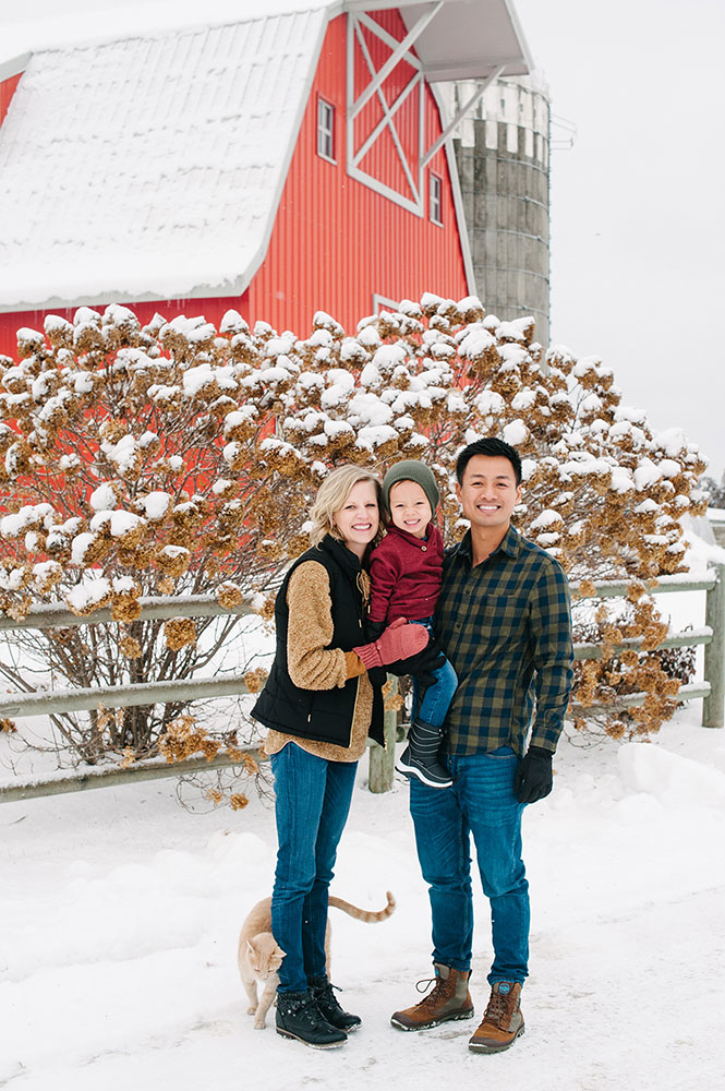 Family in front of a red barn with an orange cat in the winter