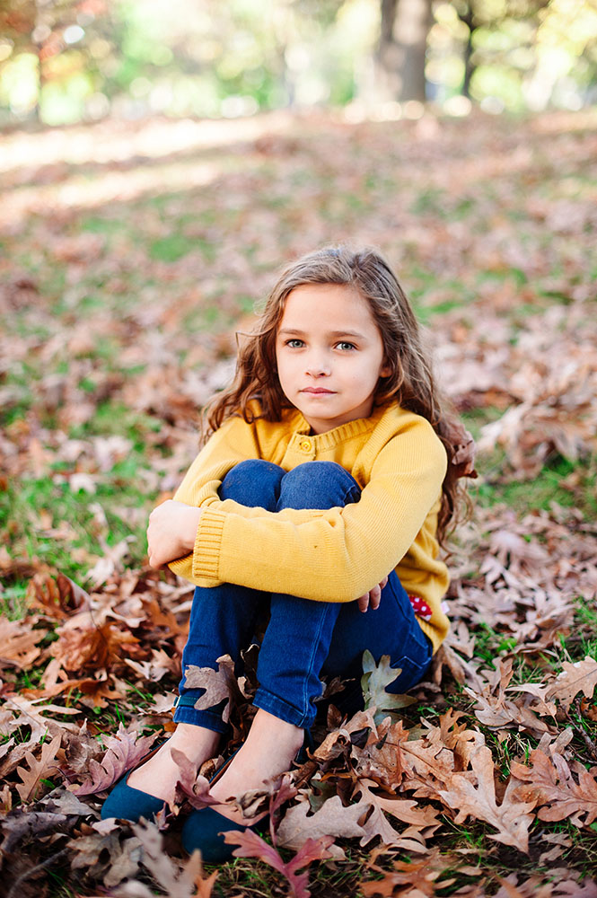 Young girl in yellow sweater and jeans in the leaves