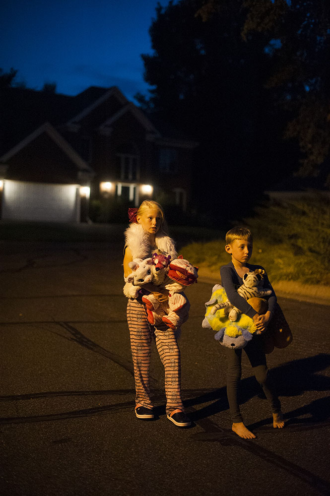 two kids on the street in the dark with stuffed animals