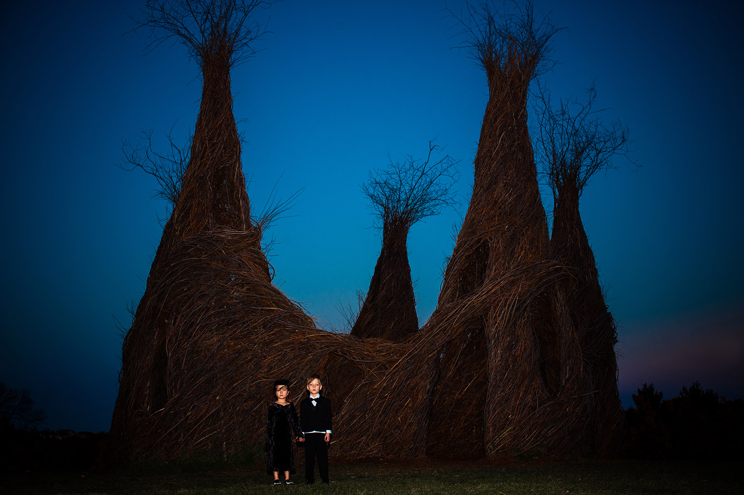 girl and boy twins dressed in black spooky attire in front of stick sculpture