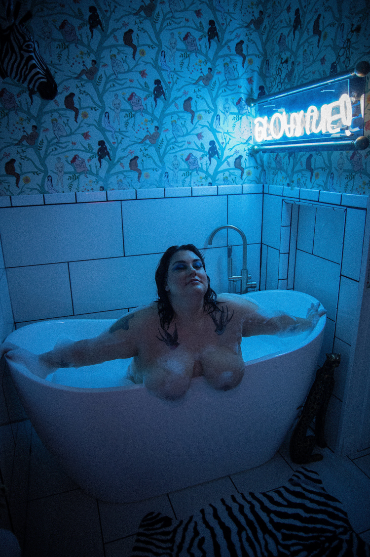 a white woman in a bathtub with blue light at the Zebra House boudoir