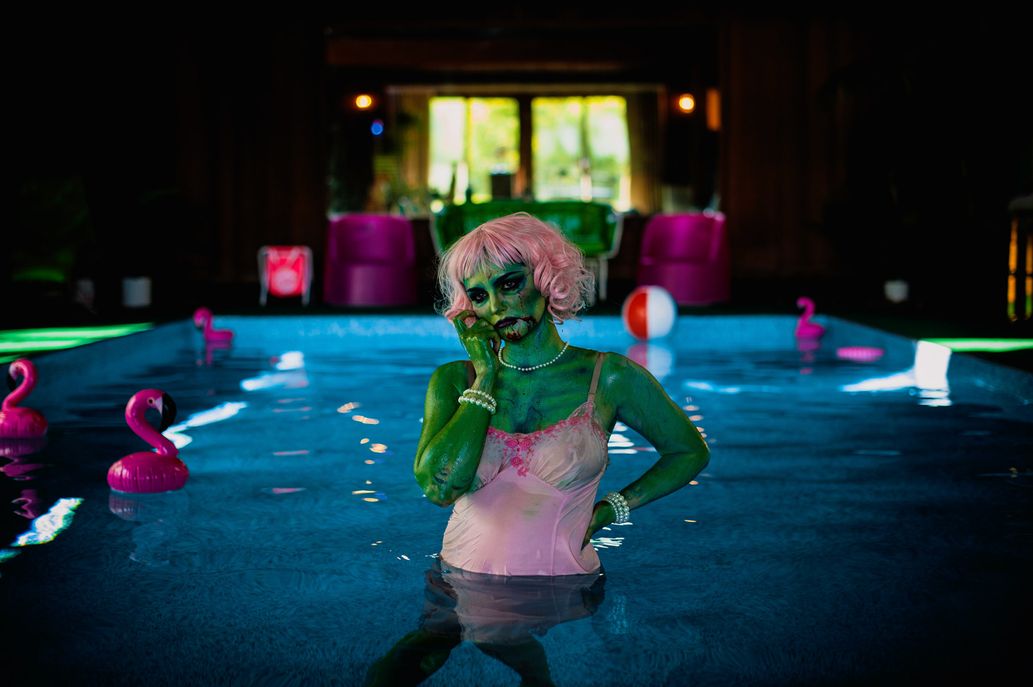 a green zombie girl with pink hair and pink nightie in a pool with pink flamingos at Grandpas pool house