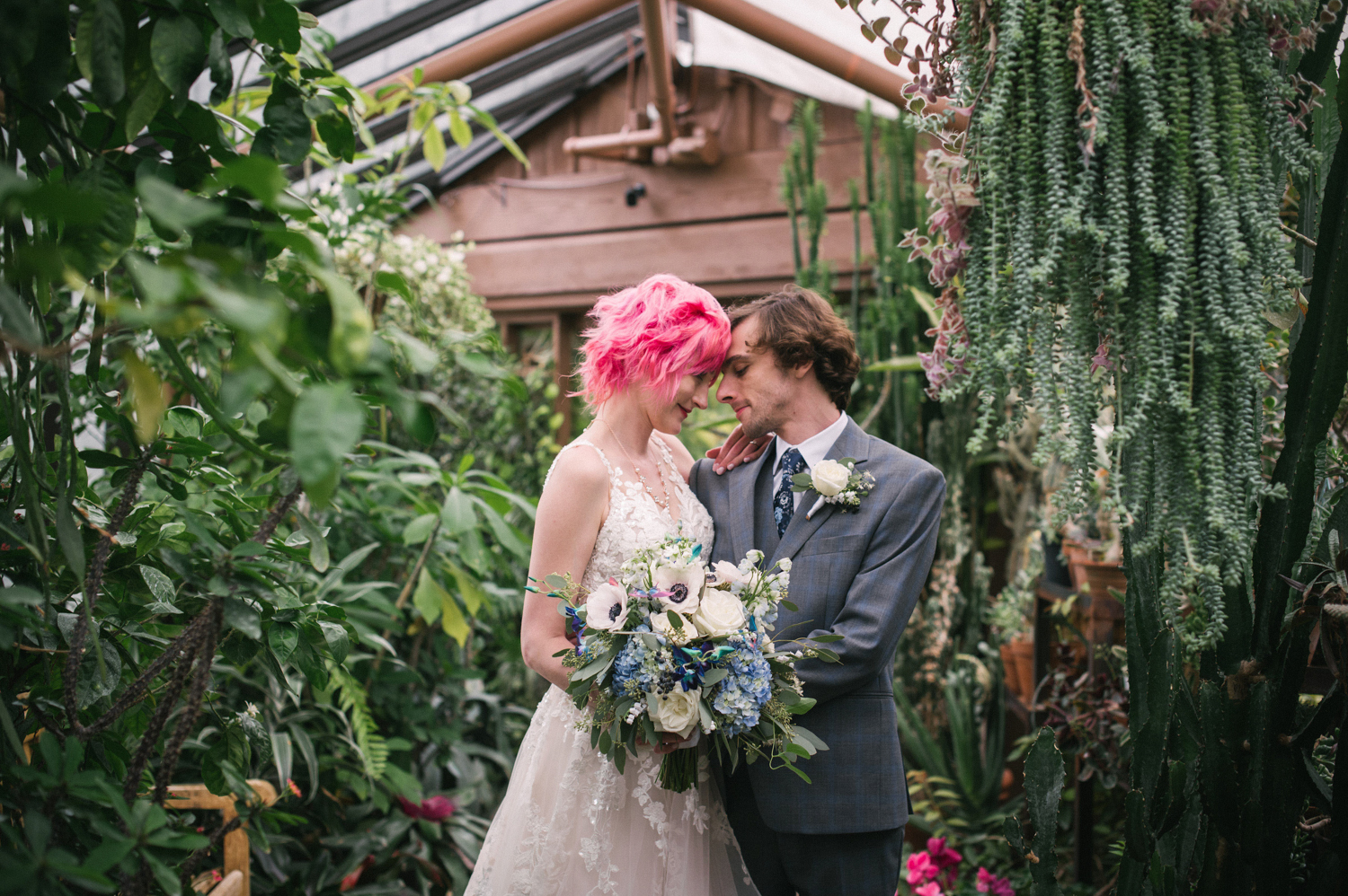 a bride with pink hair and a groom holding each other in the conservatory at the Minnesota Landscape Arboretum