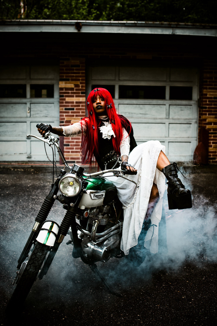 an African American woman in goth clothing and red hair on a motorcycle at the Zebra House